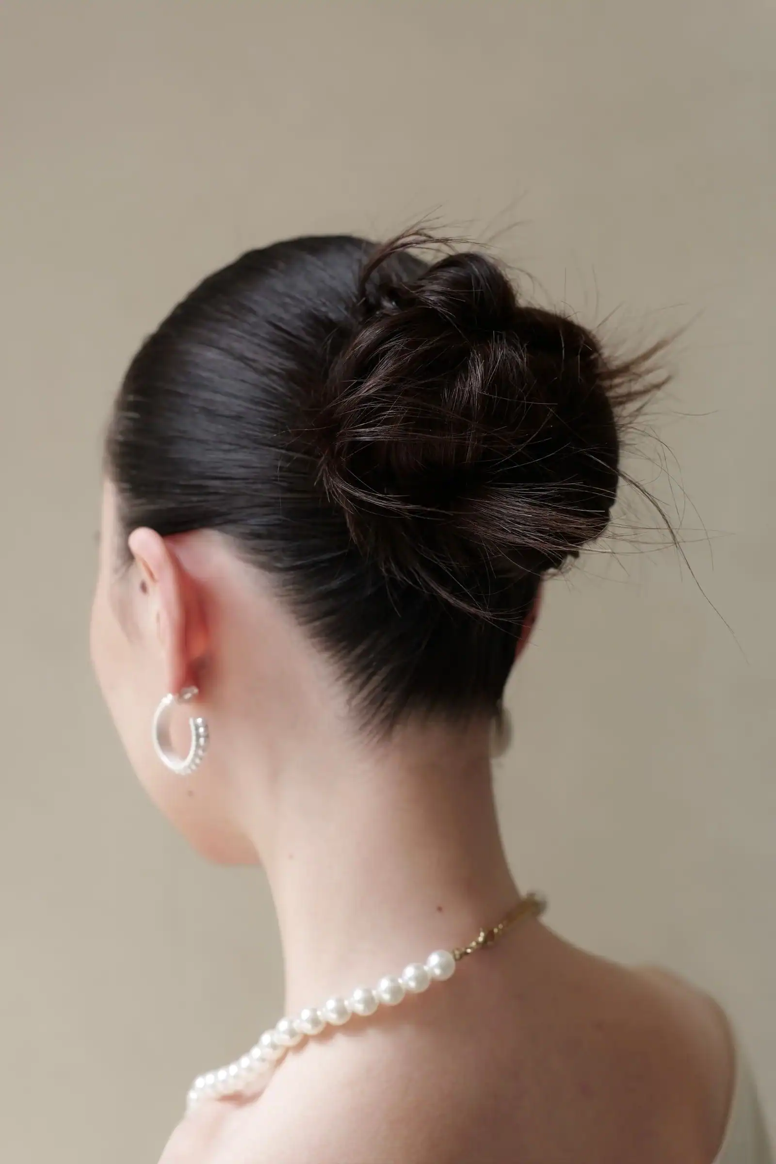 The back of a woman with a low twisted bun and a pearl necklace