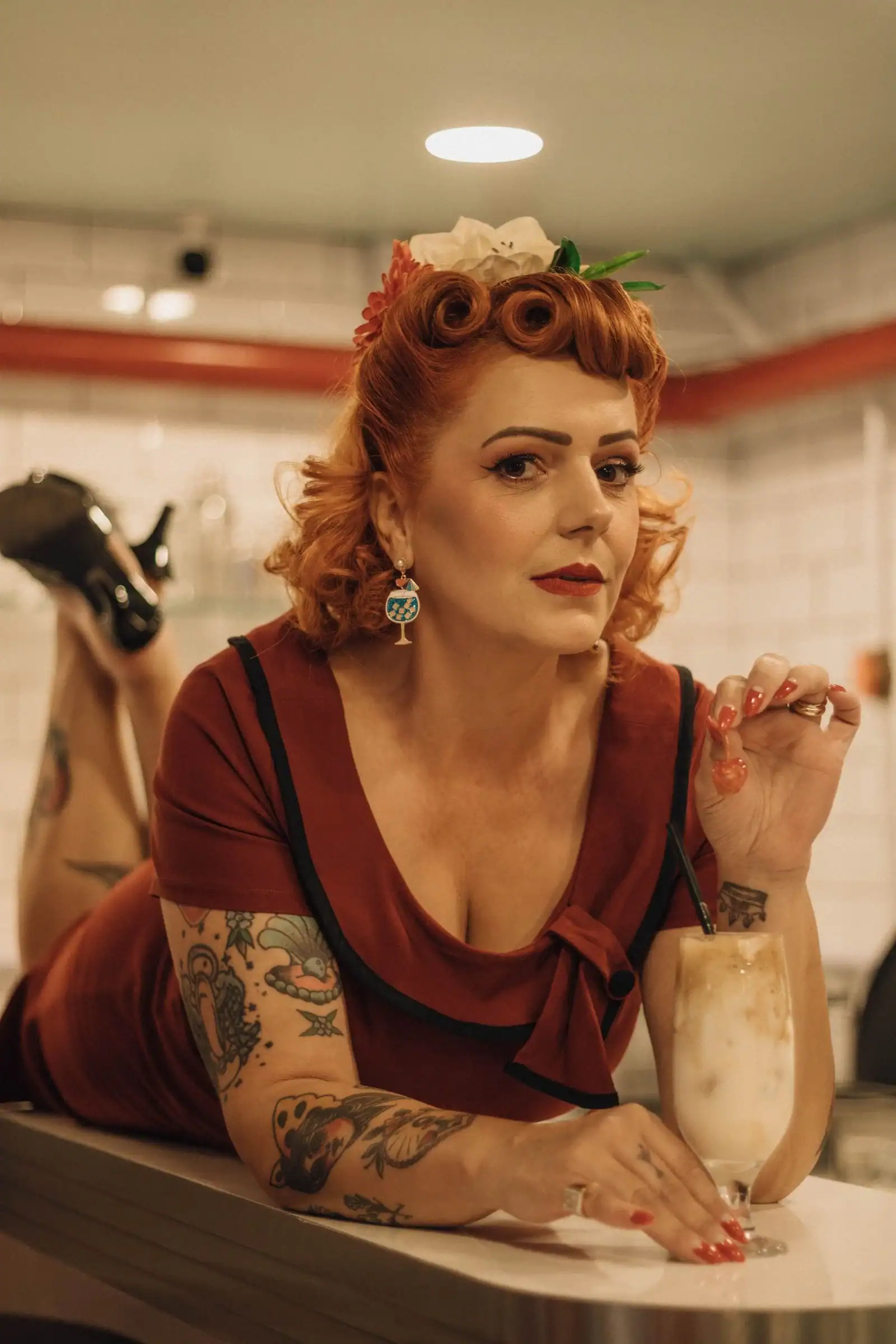 A woman with red pin-up curls and a floral hair piece in a diner