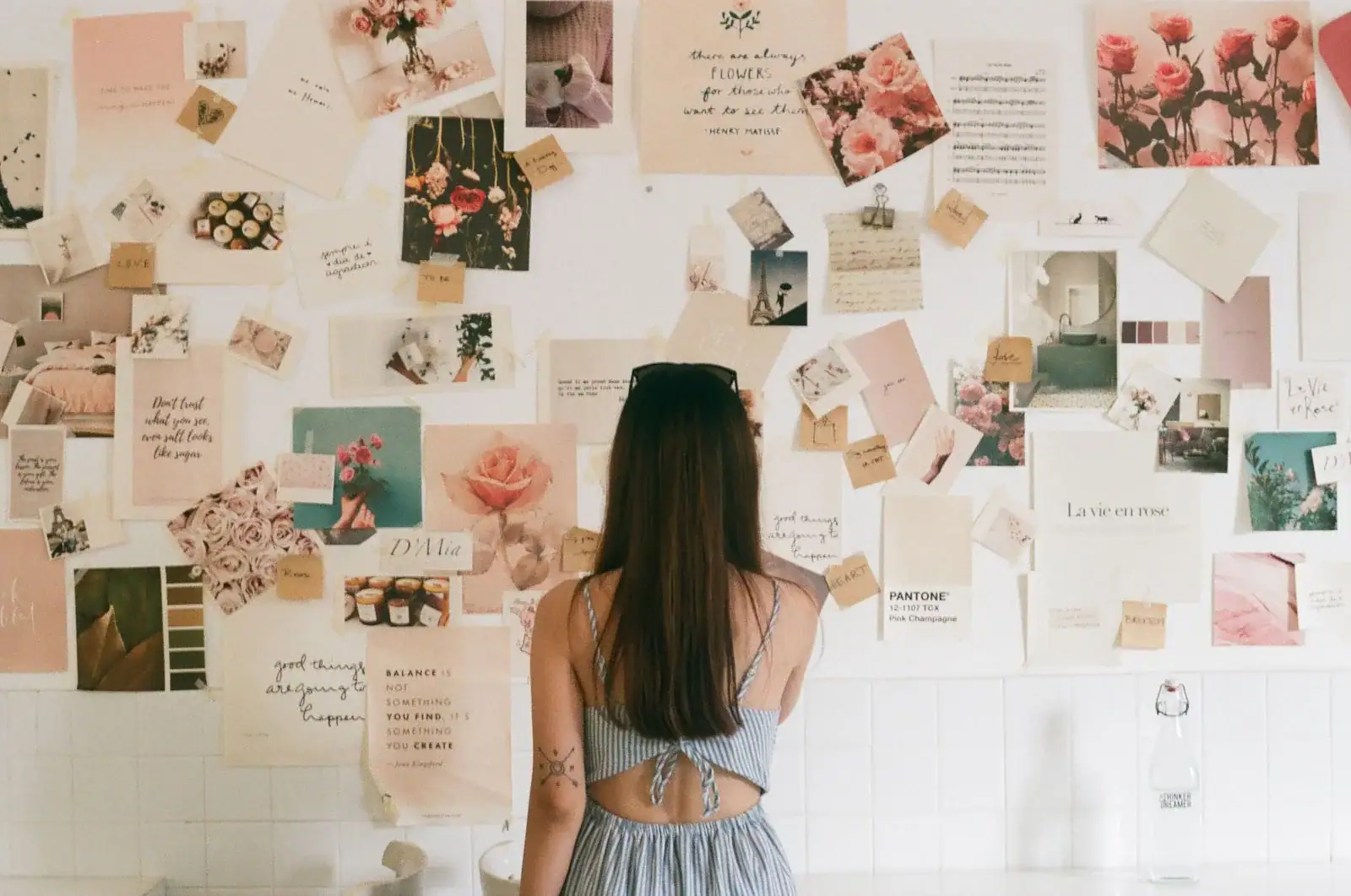 A woman looking at a wall covered with pinned photos and notes