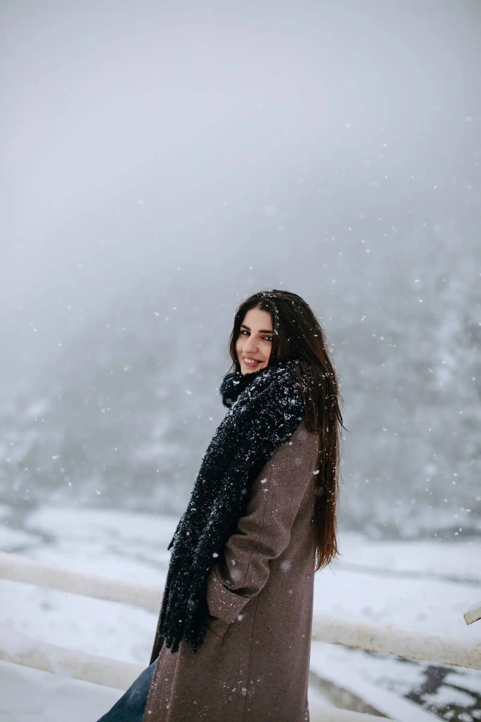 A woman in a brown coat and a black scarf in falling snow