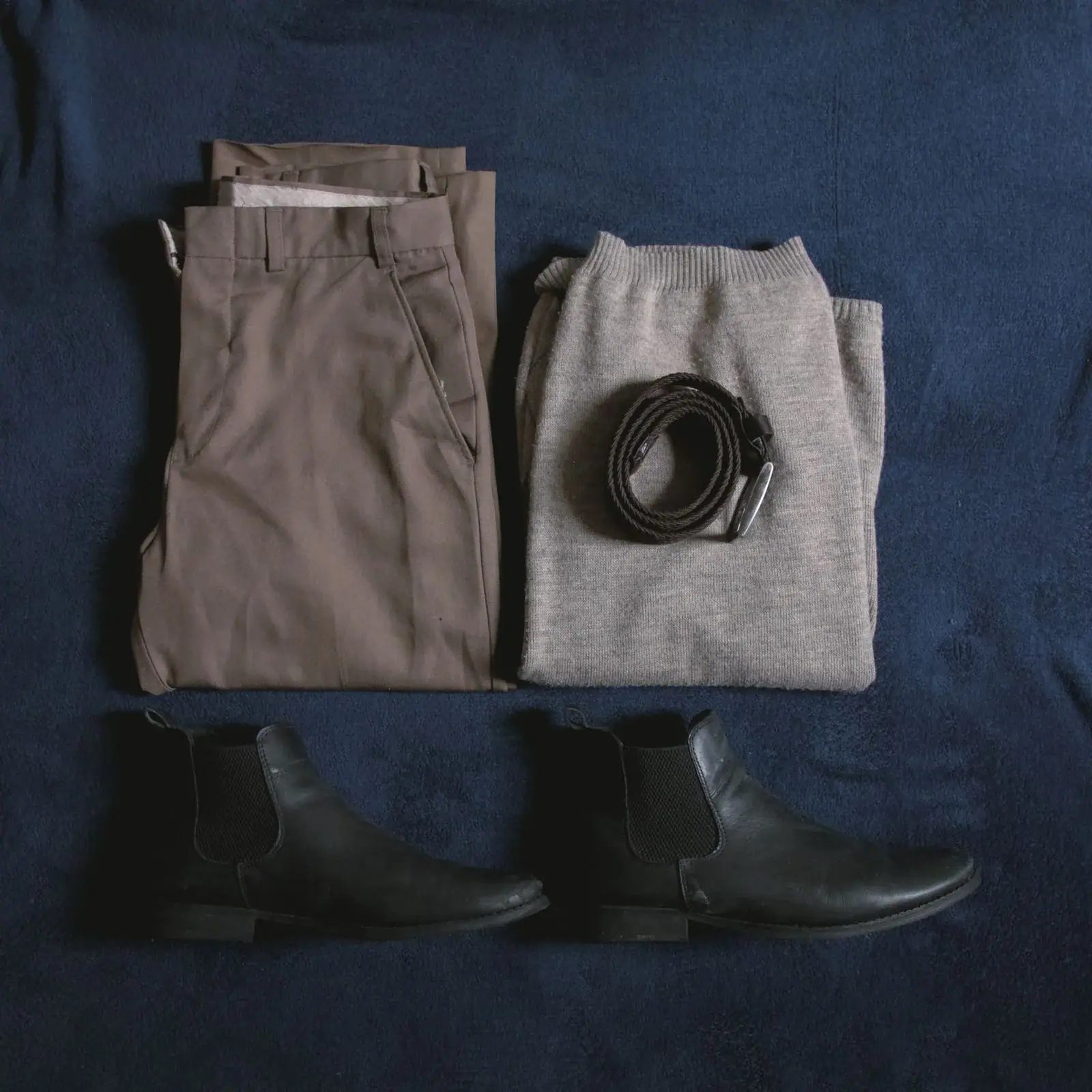 Folded trousers, a belt and black boots on a navy surface