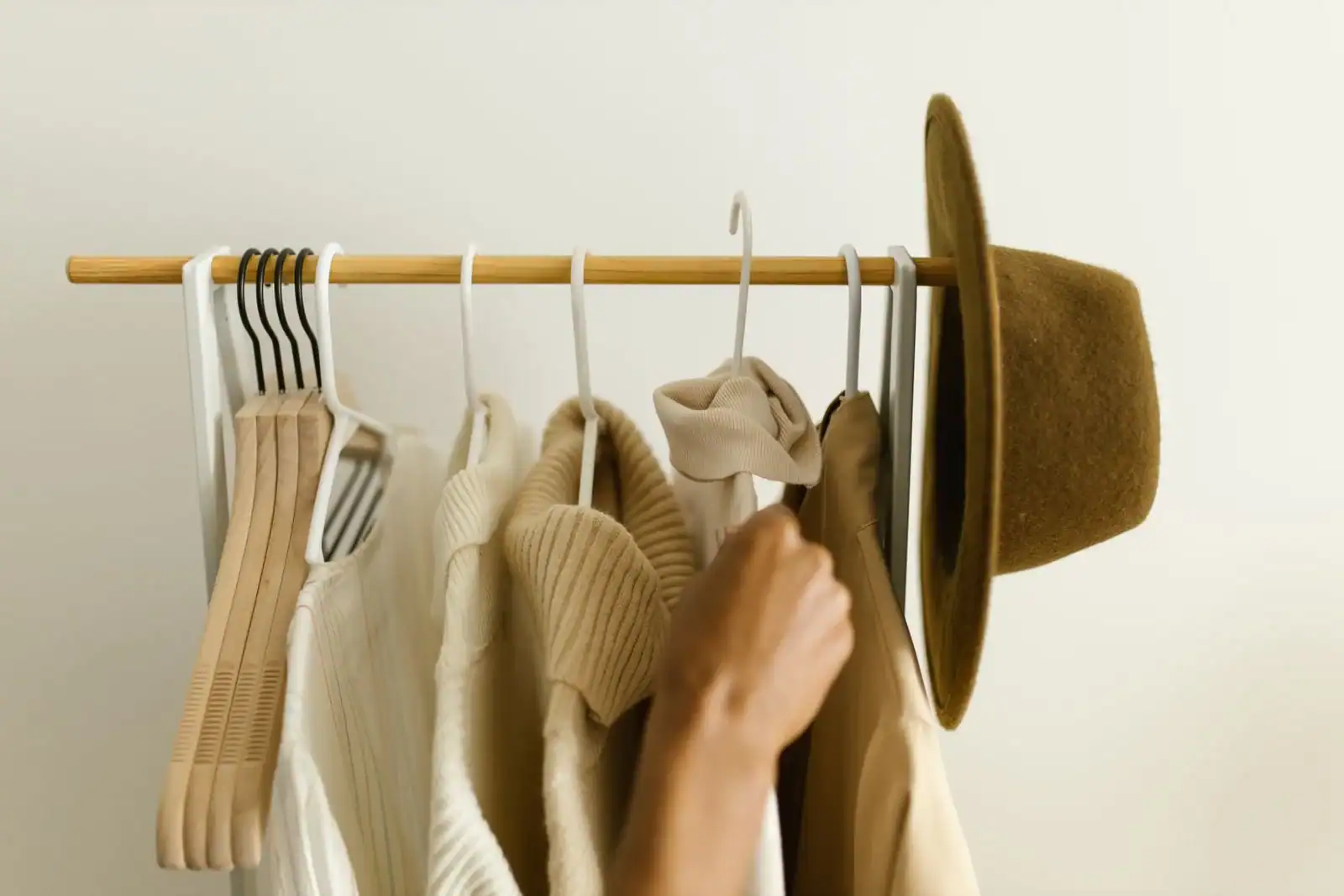 A hand choosing a neutral knit from a rail with a felt hat