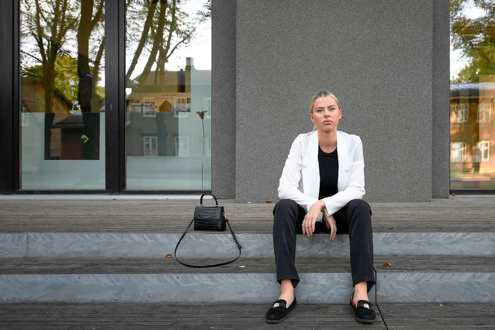A woman in a white blazer, black trousers and loafers seated on steps